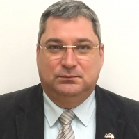 Fotogrāfija ar iestādes direktoru- vīrieti uzvalkā, baltā kreklā ar šlipsi, uz acīm brilles