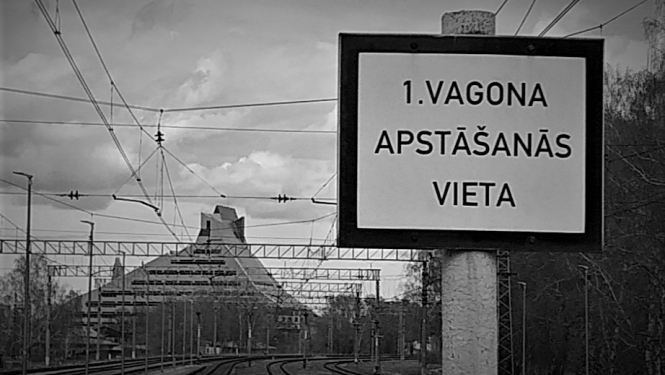 Dzelzceļa zīme. Balta plāksne ar uzrakstu melniem burtiem pirmā vagona apstāšanās vieta. Melnbalta fotogrāfija.