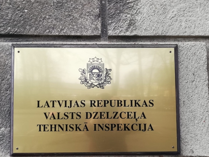 Attēls ir uz tumši pelēkas krāsas sienas ķieģeļa fona, centrā uz zelta krāsas plāksnes augšpusē attēlots “Latvijas mazais papildu ģerbonis”, bet zem tā melnā krāsā uzraksts “Latvijas republikas Valsts dzelzceļa tehniskā inspekcija”.  